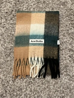 Rutig halsduk från Acne Studios - Snygg rutig halsduk från Acne Studios i mjuk ull. Färgblock i beige, blå, svart och vitt med fransar i ändarna. Perfekt accessoar för att lyfta din outfit med en trendig touch.