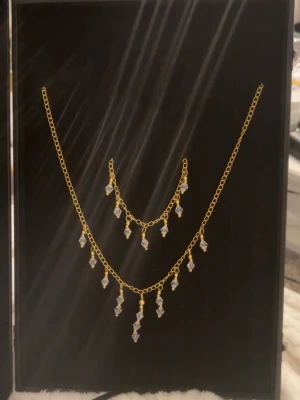 Guldfärgat halsband med pärlor med matchande armband - Snyggt halsband och matchande armband i guldfärgad metall med hängande pärlor i kristall-look. Båda går att justera hur lång man vill ha den