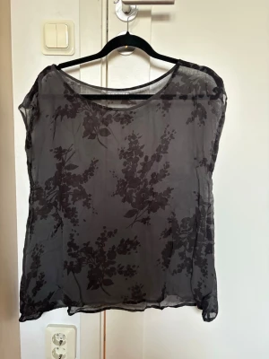 Svart blommig transparent blus - Säljer en svart transparent blus med blommigt mönster. Tunn och luftig, vilket gör den skön att bära.