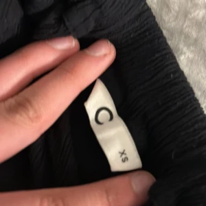 Svart långkjol med slits från Cubus - Säljer en svart långkjol från Cubus i storlek XS. Kjolen har en rak passform och en slits på sidan som ger en snygg detalj. Perfekt att styla med en croppad topp eller stickad tröja.