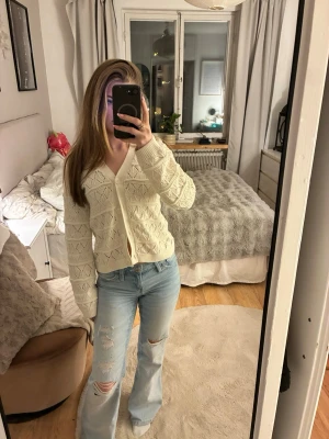 Krämvit stickad kofta med mönster - Säljer en krämvit stickad kofta med v-ringning och fina hålmönster. Koftan har långa ärmar och knappar framtill. Perfekt att slänga över en topp för en avslappnad look. Materialet känns mjukt och bekvämt.