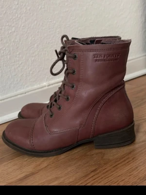 Vinröda läderkängor Ten Points - Snygga vinröda kängor från Ten Points i modellen Pandora. Kängorna är i äkta läder med snörning framtill och dragkedja på sidan. Mörk sula och klassisk design som passar perfekt till höst och vinter. Märkeslogga på sidan .