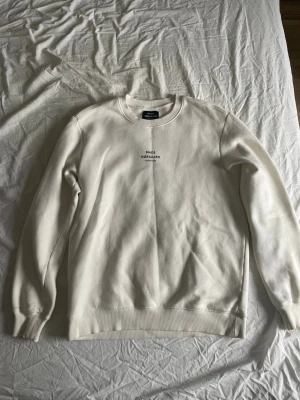 Vit sweatshirt från Mads Nørgaard - Säljer en stilren vit sweatshirt från Mads Nørgaard med rund halsringning och diskret logotyp på bröstet. Tröjan har ribbade muddar vid ärmslut och nederkant, perfekt för en clean och avslappnad look.