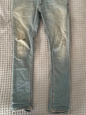 Ljusblå dondup jeans med slitningar - Säljer ett par ljusblå dondup jeans med slitningar på vänster lår och bakfickor. Jeansen har klassisk femficksdesign och är tillverkade i denim med en snygg tvättad look. Perfekta för en avslappnad och trendig stil.