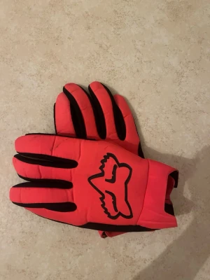 Röda Fox handskar med svart logga -  röda moped handskar från Fox med svart logga på ovansidan och svarta detaljer på fingrarna. Insidan är svart med greppytor och röd accent på tummen.