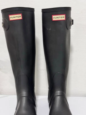 Svarta höga stövlar från Hunter - Säljer ett par klassiska svarta höga stövlar från Hunter. Tillverkade i slitstarkt gummi med ikonisk logga framtill. Perfekta för regniga dagar och har en tidlös design som funkar till många olika stilar.