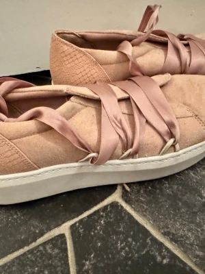 Beiga sneakers med satinband - Unika sneakers i beige mocka med detaljer i ormmönstrad textur på hälen och breda satinband som snörning. Skorna har en vit platåsula och en stilren, modern design som sticker ut. Perfekta för dig som vill ha något annorlunda och trendigt.