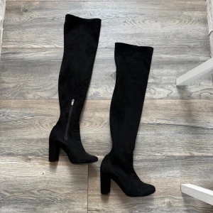 Svarta overknee stövlar i mocka - Säljer ett par svarta overknee stövlar med chunky klack och dragkedja på insidan. Stövlarna är tillverkade i mjuk mocka och har en stilren, hög siluett som passar perfekt till olika outfits. 