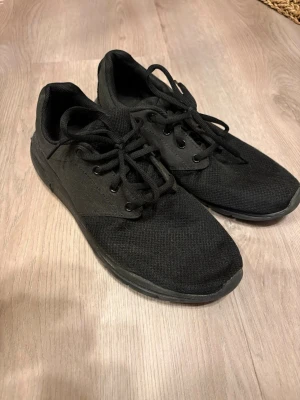 Helvita svarta sneakers från Nike - Säljer ett par helsvarta sneakers från Nike med klassisk låg profil. Skorna har ovandel i mesh och textil, snörning och diskret swoosh på sidan. Perfekta för dig som gillar stilrena och bekväma skor till vardags. Sulan är svart och ger bra grepp.