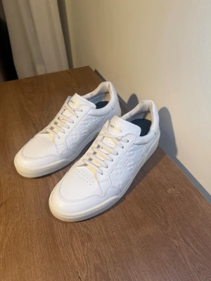 Vita Sandro sneakers i läder - Stilrena vita sneakers från Sandro i läder med diskret och snyggt mönster på sidorna. 