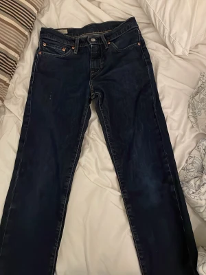 Mörkblå Levi's jeans straight fit - Snygga mörkblå jeans från Levi's med klassisk femficksdesign och raka ben. Jeansen har tydliga kontrastsömmar och en brun läderpatch bak i midjan. Tillverkade i slitstark denim, perfekta för en avslappnad och cool stil.