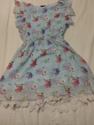 Blommig ljusblå klänning KappAhl - Supersöt ljusblå klänning från KappAhl med blommigt mönster i rosa, lila och rött. Klänningen har volangärmar och spetsdetalj nertill. Perfekt för sommarens alla tillfällen!