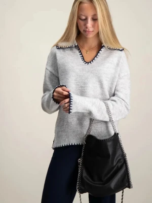 Ljusgrå stickad tröja med blå detaljer - Ljusgrå stickad tröja med v-ringning och mörkblå dekorativa kanter vid hals, ärmslut och nederkant. Tröjan har en avslappnad passform och långa ärmar, perfekt för att hålla sig varm under kyliga dagar. Strl 146/152 men passar xs/s