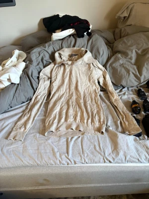 Beige stickad polotröja från dressman - Säljer en beige stickad polotröja med lång ärm och ribbade muddar. Tröjan har en mjuk och tunn kvalitet, perfekt för lager på lager. Enkel och stilren design utan synliga loggor eller mönster.