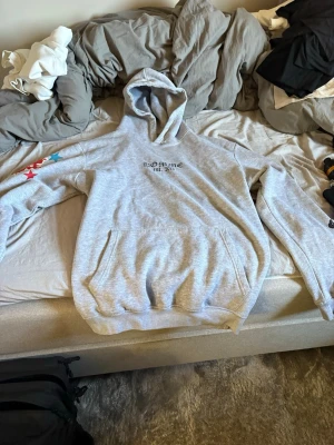 Grå Bohooman hoodie med tryck - Snygg grå hoodie från Bohooman med tryck på bröstet och stora färgglada kors på ryggen och ärmarna. Klassisk känguruficka framtill och huva. Perfekt för dig som gillar streetwear och vill sticka ut med unika detaljer.