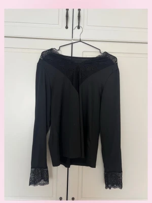 Svart långärmad topp med spetsdetaljer - 💓Snygg svart långärmad topp med spetsdetaljer vid halsringning och ärmslut. Toppen har en elegant och feminin look med transparent spets som ger extra stil. Perfekt för dig som vill ha något lite extra till din outfit.💕