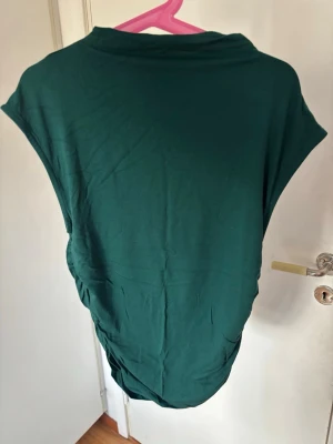 Mörkgrön ärmlös topp  med rynk - Snygg mörkgrön topp i mjukt material med ärmlös design och rynkade detaljer på sidan. Passar till många olika stilar och är superbekväm.