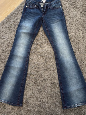 Blå bootcut jeans från Gina Tricot - Säljer ett par blå bootcut jeans från Gina Tricot i storlek XS 14+. Jeansen har snygga slitningar framtill, röda kontrastsömmar.