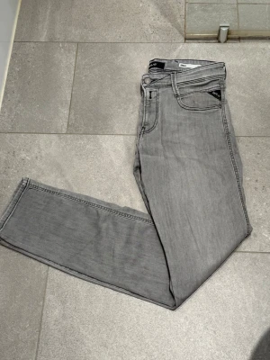 Grå replay anbass jeans - Snygga grå jeans från Replay med klassisk femficksdesign och raka ben. Jeansen har en diskret tvättad look och är tillverkade i mjukt denimtyg som ger en skön känsla. Perfekta för en avslappnad och trendig stil. Jeansen är i nyskick och endast använda 3 gånger, dessa är köpta på Joel i Borås för 1800kr, Storleken är  30/32, mitt pris är 500kr, tveka inte med att höra av er vi frågor eller funderingar 😊