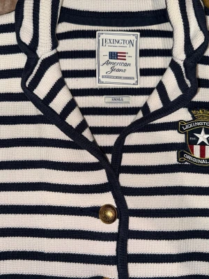 Randig stickad cardigan från Lexington - Snygg marinblå och vitrandig tröja med guldfärgade knappar och broderad logga på bröstet. Perfekt till både vardag och finare tillfällen.   