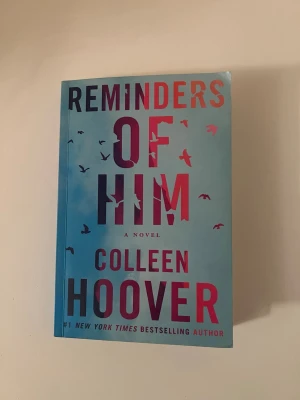 Reminders of Him av Colleen Hoover - En roman av Colleen Hoover med blått omslag och fågelmotiv. Boken handlar om en ung mamma som kämpar för att återförenas med sin dotter efter ett fängelsestraff. Finns vikta kanter