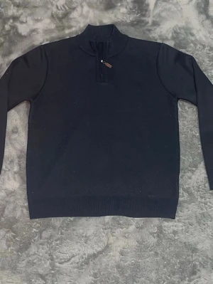 Marinblå stickad halvzip tröja - Marinblå stickad tröja med halv dragkedja och ståkrage. Tröjan har långa ärmar och ribbade muddar vid ärmslut och nederkant. Perfekt för lager på lager och enkel att matcha med olika outfits