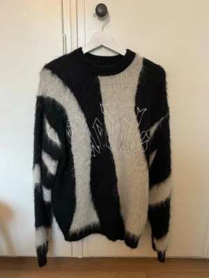 Stickad tröja Beyond Medals  - Säljer en stickad tröja från Beyond Medals i storlek S. Tröjan har ett svart och vitt/grått abstrakt mönster, rund halsringning och är gjord i ett fluffigt, mjukt material av alpacka päls 