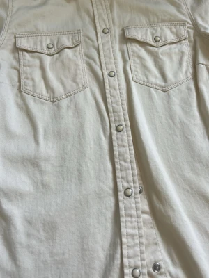 Skjorta från Vero Moda XS - Snygg beige skjorta från Vero Moda i storlek XS. Skjortan har två bröstfickor med lock och tryckknappar, klassisk krage och raka sömmar. Perfekt för dig som gillar en clean och stilren look.