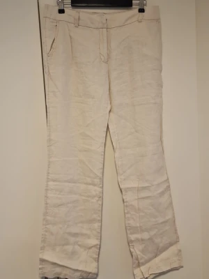 Beiga linnebyxor med raka ben - Säljer ett par stilrena beiga linnebyxor med raka ben och klassisk passform. Byxorna har fickor fram, bälteshällor och stängs med dragkedja och knapp. Perfekta för en avslappnad och trendig look under varmare dagar.
