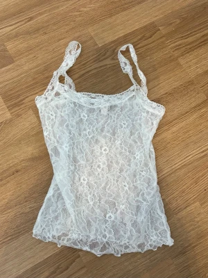 Vit spets linne - Säljer en vit, ärmlös linnetopp i genomskinlig spets med blommigt mönster. Toppen har smala axelband och en feminin, figurnära passform. Perfekt att styla lager på lager eller till ett par jeans. Pris 70kr. Storlek XS. Enbart testad.