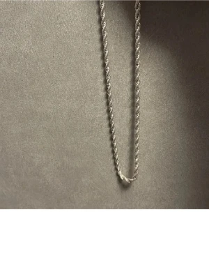  Cordell hanlsband(Rostfritt stål) - Snyggt halsband i silverfärg med tvinnad kedja som ger en stilren och modern look. Perfekt att bära som det är eller att kombinera med andra smycken för en personlig stil. Materialet ser ut att vara metall med en glansig finish.