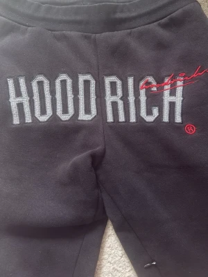 Svarta mjukisbyxor från Hoodrich - Säljer ett par svarta mjukisbyxor från Hoodrich med stor broderad logga i vitt och grått samt röd detalj framtill. Byxorna har många fickor. För hela settet 700 för en av dem pris kan diskuteras!