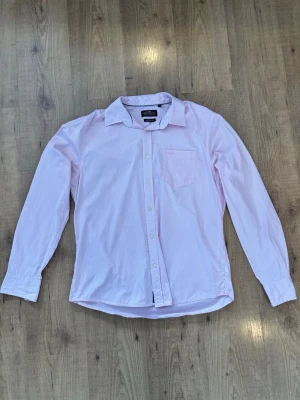 Ljusrosa skjorta från Hampton Republic  - Klassisk ljusrosa skjorta från Hampton Republic med lång ärm, bröstficka och knappar framtill. Skjortan har en avslappnad pasform och är tillverkad i mjuk bomull. Perfekt för en clean och stilren look. Passformen är Regular fit. 