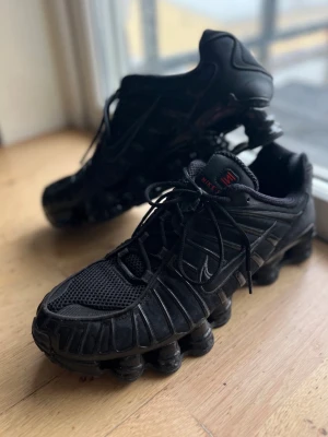Nike Shox TL  - Nike Shox TL sneakers i helsvart med mesh och syntetiska paneler. Skorna har den ikoniska fjädrande Shox-sulan och diskreta röda detaljer på plösen. Swoosh-logga på sidan och snörning framtill. Riktigt futuristisk vibe och grym komfort. Används 2 gånger. Allt i dm. ÄKTA