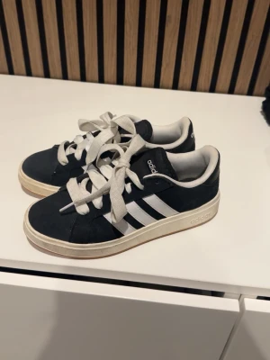 Svarta Adidas sneakers  - Snygga svarta Adidas sneakers med klassiska vita ränder på sidorna och vit sula. Skorna har vita skosnören och låg profil. Se bild på smuts på mellansulan. 