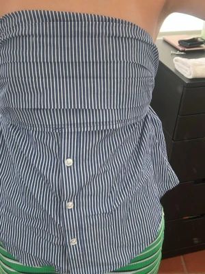 Randig blå axelbandslös tubtopp - Säljer en snygg blå tubtopp med vita ränder och knappar framtill. Toppen är axelbandslös och kommer från newyorker. St Xs