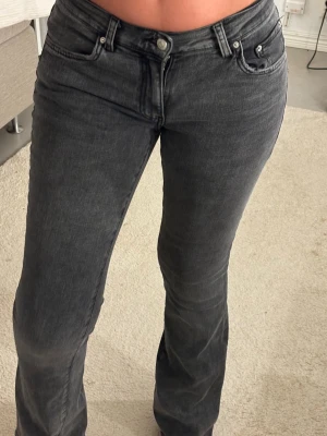 Mörkgråa bootcut jeans mid waist - Snygga mörkgråa bootcut jeans med mid waist och klassisk femficksdesign. Jeansen har en lätt tvättad look och stängs med knapp och dragkedja. Perfekta för en trendig och avslappnad stil. 