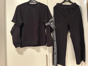Svart loungewear-set med textdetaljer - Säljer ett svart loungewear-set med långärmad tröja och matchande byxor. Setet har vita textband med 'STATUS STYLE' längs ärmar och byxben. Perfekt för chill dagar hemma. Mjuk och bekväm passform.