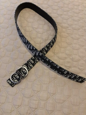 Cd belt  - Snyggt svartvitt bälte med tydligt logomönster och dubbla silverfärgade D-ringar som spänne. Bältet har en klassisk form och är gjort i skinn med textil på ovansidan. Perfekt för att lyfta vilken outfit som helst.