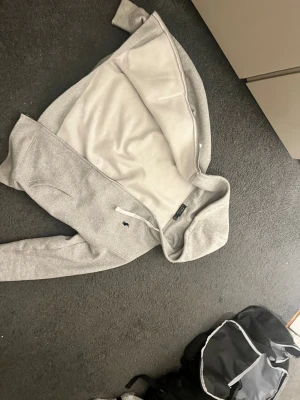 Grå  Polo Ralph Lauren - Zip funkar inte men går att laga,Snygg gråmelerad hoodie från Polo Ralph Lauren. Klassisk huva med vita snören, två fickor fram och den ikoniska lilla loggan broderad på bröstet. Perfekt för en avslappnad och stilren look.