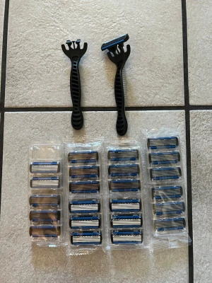 Rakset med 24 extra rakblad, med 6 blad  - Säljer ett rakset med två svarta rakhyvlar i plast och flera utbytbara rakblad. Rakbladen har blå och silverfärgade detaljer och levereras i plastförpackningar. Perfekt för dig som vill ha många blad tillgängliga för en smidig rakning.