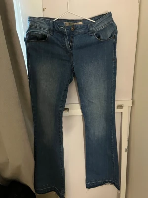 Blå bootcut jeans - Säljer ett par blå bootcut jeans med klassisk femficksdesign och rå kant nertill. Jeansen har en snygg tvätt med lätt slitning framtill och bakfickor med dekorativ söm. Perfekta för dig som gillar en avslappnad men trendig look. Korta i längden så passar nån som är runt 160