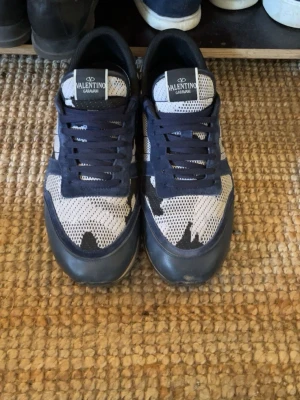 Mörkblåa Valentino Garavani Rockrunners - Snygga sneakers från Valentino Garavani i blått och vitt med coolt kamouflagemönster. Skorna har snörning och ovandel i mesh och syntet för en sportig vibe. Köpt förra vintern på en app som heter vestaire (en second hand app för exclusiva märken) men har inte använt då mycket då jag tycker om ett annat par av mina skor mer, skriv för frågor, pris är diskuterbart som alltid, glad påsk allihopa 🐣❤️