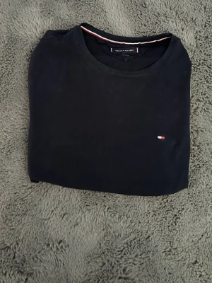 Tommy Hilfiger Slim Fit - •	Märke: Tommy Hilfiger •	Modell: Extra Slim Fit •	Storlek: S •	Färg: Djup mörkblå •	Skick: Mycket fint skick, väl omhändertagen •	Material: Mjuk och högkvalitativ bomull med skön    känsla mot huden •	Passform: Elegant slim fit som ger en modern och skräddad silhuett •	Design: Minimalistisk med diskret broderad logotyp på bröstet •	Stil: Tidlös och mångsidig – passar lika bra till en uppklädd som avslappnad look •	Perfekt för dig som söker ett stilrent premiumplagg med klassisk design