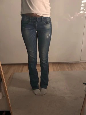 Blå bootcut jeans med slitningar - Snygga blå bootcut jeans med lätt slitna detaljer på låren och knäna. Klassisk femficksmodell och låg midja. 