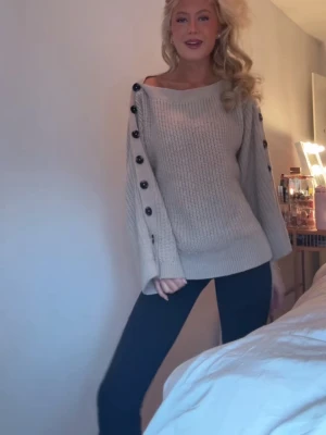 Beige stickad tröja med knappar - Snygg beige stickad tröja med bred halsringning och stora svarta knappar längs hela ärmarna. Super skick, helt slutsåld!! Skriv för egna bilder💕💕💕