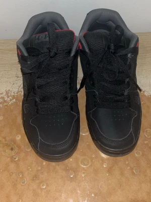 Svarta DC sneakers med röda detaljer - Snygga svarta sneakers från DC med röda detaljer och grå insida. Skorna har klassisk DC-logga på sidan, meshpaneler för extra ventilation och robust sula. Perfekta för dig som gillar streetwear och skate-stil. Vid snabb försäljning 500kr