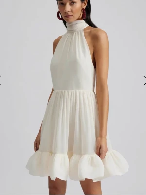 Vit kortklänning med volang och knyt - Säljer nu min drömmiga miniklänning från By Malina, perfekt för studenten, examen eller sommarens alla fester. Klänningen är i nyskick då den endast burits vid ett enstaka tillfälle 