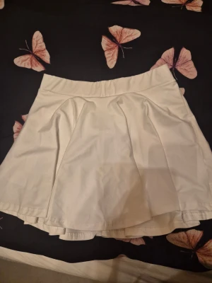 Vit skort - Supersnygg vit skort med plisserad kjoldel och inbyggda shorts. Skorten har bred midjeresår och är gjord i ett mjukt, stretchigt material som ger en bekväm passform. Perfekt för en trendig och sportig look. Finns en ficka under kjolen där man kan lägga tex mobil.