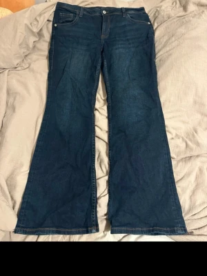 Mörkblå bootcut jeans - Säljer ett par mörkblå bootcut jeans med klassisk femficksdesign och normal midja. Jeansen har vida ben och är tillverkade i mjukt denimtyg som ger en skön passform. Perfekta för dig som gillar retrostil och vill ha ett par jeans som sticker ut.